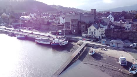 idyllic conwy castle and harbour fishing town boats on coastal waterfront aerial left dolly over pier