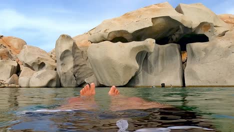 perspectiva personal de las piernas y los pies del hombre relajándose mientras flota en aguas tranquilas de la laguna lavezzi en la isla de córcega en francia