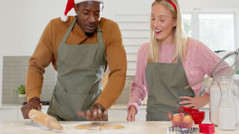 christmas time, diverse couple baking holiday cookies together in kitchen, wearing hats and aprons