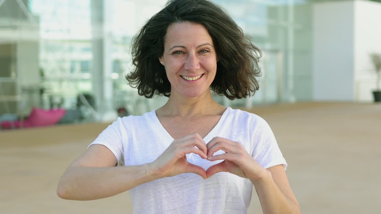 atractiva morena sonriente haciendo forma de corazón con las manos.