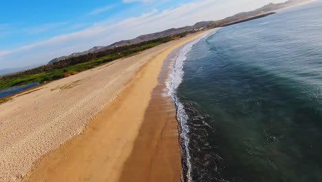 fpv drone shot over wild coastal sandy beach and ocean waves in baja region mexico, flying fast along shore and turquoise sea water, seaside landscape