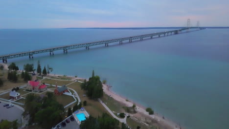 Cinematic-aerial-drone-Mackinaw-Bridge-lighthouse-Michigan-sunset-dusk-purple-pink-stunning-Great-Lakes-landscape-mid-summer-up-north-Petoskey-Harbor-Springs-peaceful-cars-cross-bridge-forward-motion
