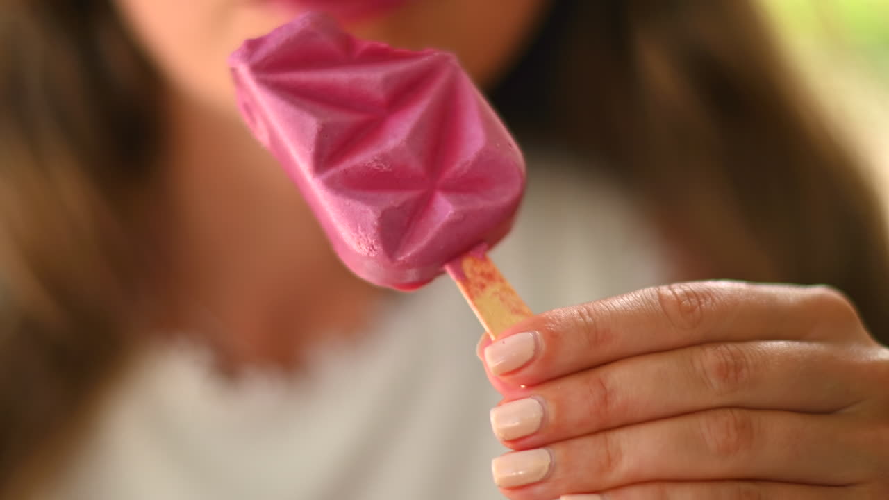 Donna bruna che mangia un gelato rosa in un bar, alla luce del giorno