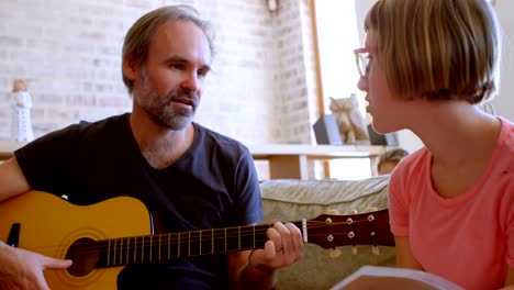 un padre ayudando a su hija a tocar la guitarra en la sala de estar 4k