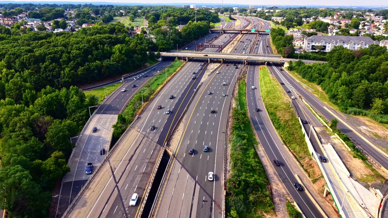 Overhead view of highway traffic and interchange. High angle drone shot of busy roadways cutting through lush forest and suburban housing. Garden State Parkway
