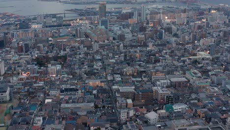 Kobe-Aerial-reveal-tilt,-lights-of-city-coming-on-after-sunset