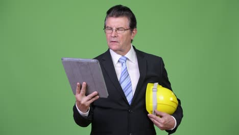 Senior handsome businessman as engineer using digital tablet