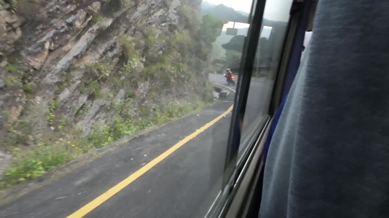 POV bus ride through Nepal's rugged interior. Camera facing out of the side window. Motorcycle is driving in front