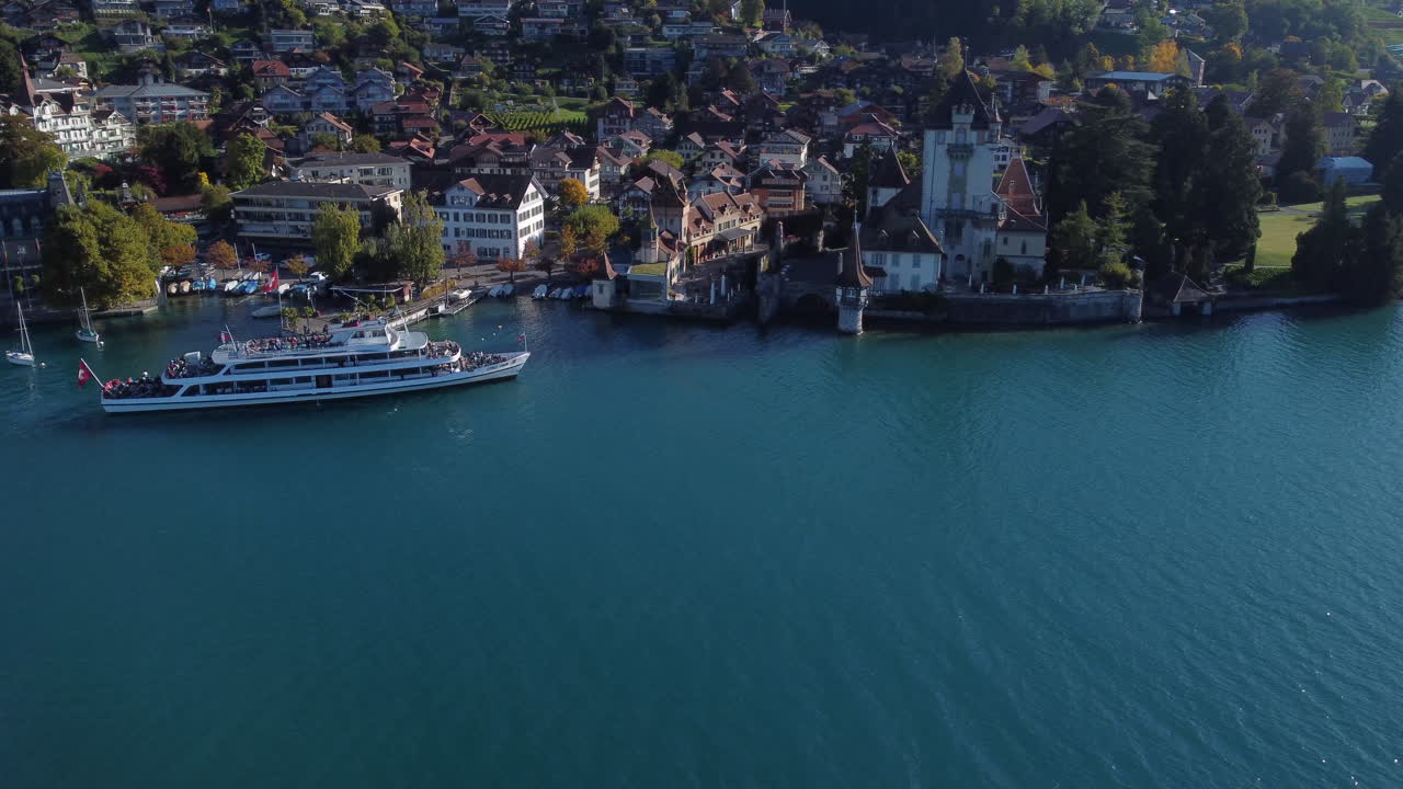 화창한 날 스위스에서 오버호펜 성(oberhofen castle) 위로 환상적인 항공 샷과 부두에 접근하는 해안과 배를 볼 수 있습니다.