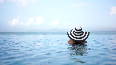 Mujer-Con-Sombrero-De-Sol-A-Rayas-En-La-Piscina-Mirando-A-Otro-Lado-De-La-Cámara