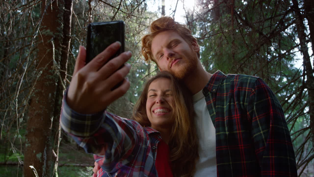 una pareja tomando selfies con su teléfono inteligente en el bosque.