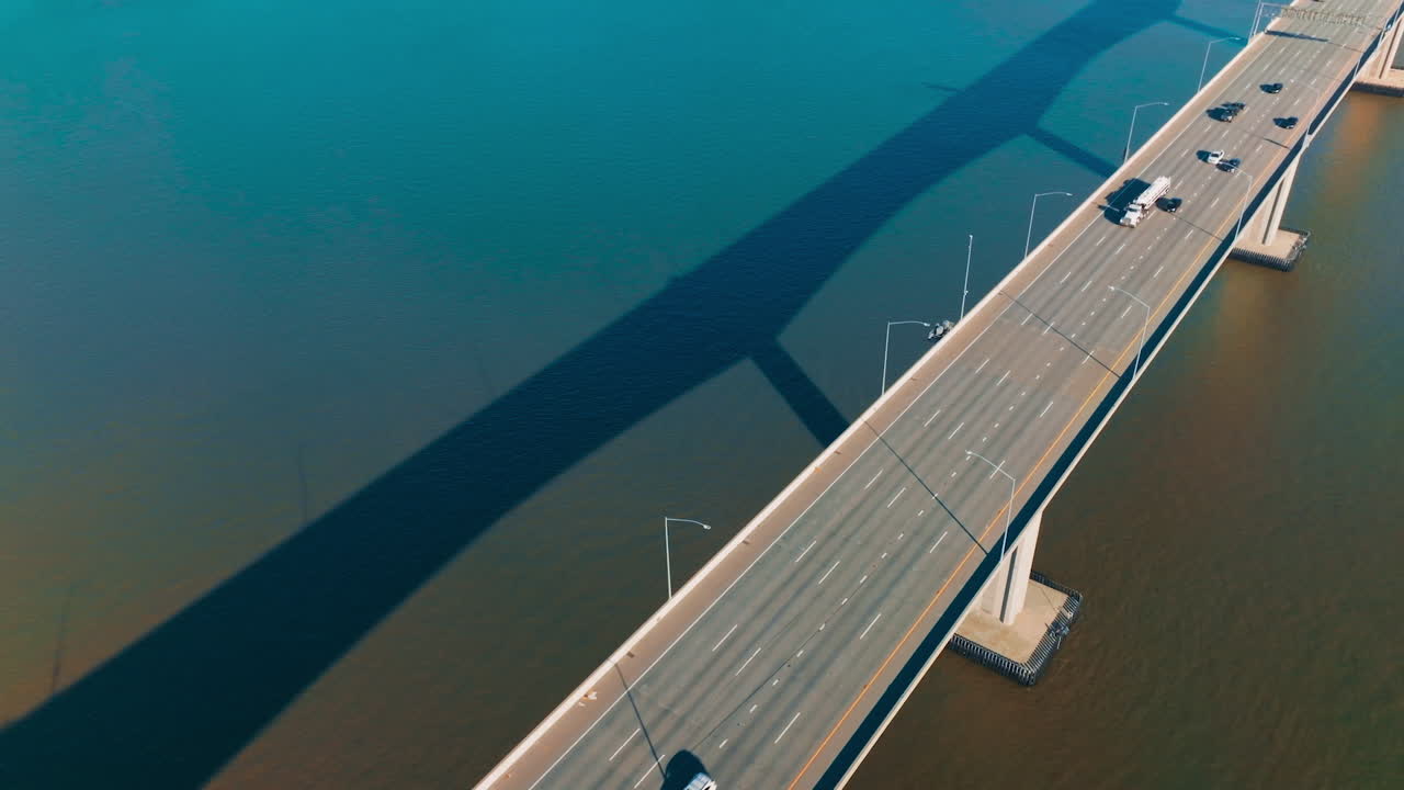 Automobile bridge with one-way multi-lane road. Transport moving by the bridge over the calm blue water. Top view.