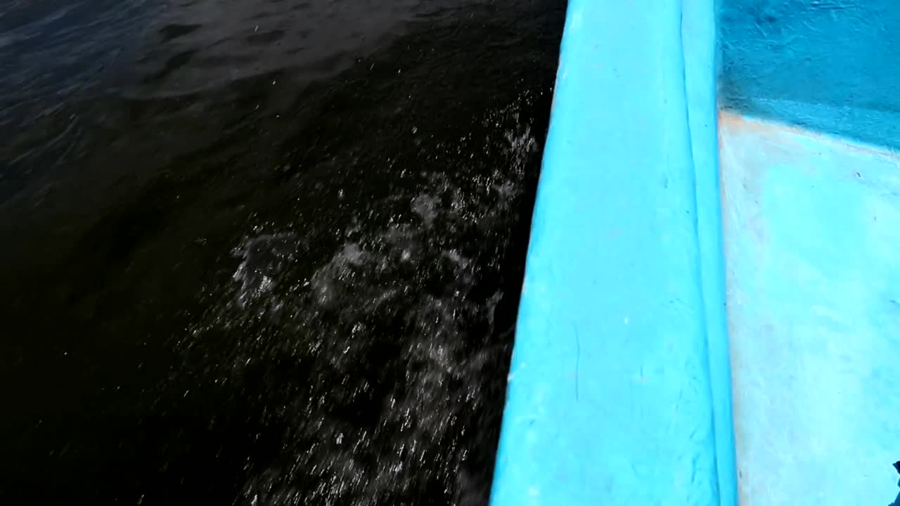 captura de detalle del costado de una lancha de fibra azul que navega mientras las olas salpican