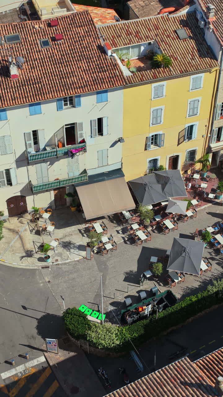 Aerial drone view of Antibes Old Town square with outdoor cafes, parasols, and historic Mediterranean buildings near the ramparts. Vertical