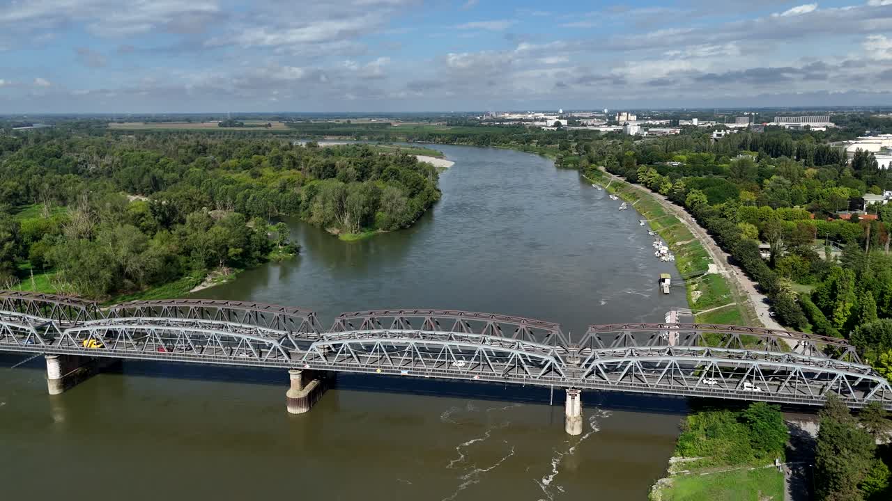 Drone push in over the large iron truss bridge crossing the Po River, connecting Cremona (Lombardy) and Castelvetro Piacentino (Emilia Romagna), with riverbanks lined by greenery