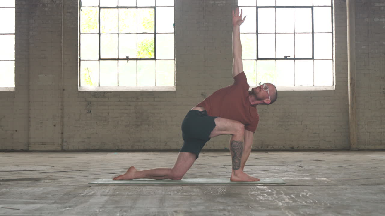Man in an industrial warehouse practicing yoga, the pose of inverted low lunge.