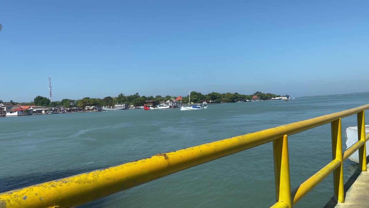 Thuyền bè di chuyển trên dòng sông yên bình, phía sau là một ngôi làng ven biển.