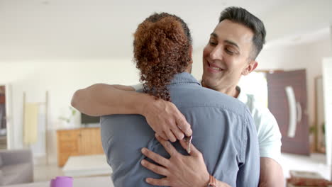 feliz pareja gay diversa con llaves de una nueva casa abrazándose en la sala de estar, en cámara lenta