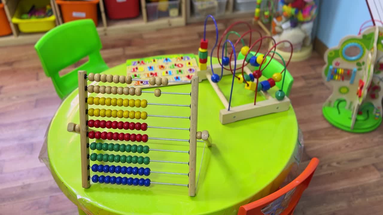 Bright 4K footage of a preschool learning setup with a wooden abacus, bead maze, and alphabet puzzle on a vibrant table. Ideal for educational, childcare, or early learning content.