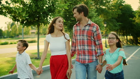 padres sonrientes y niños caminando en el parque. familia alegre cogida de la mano