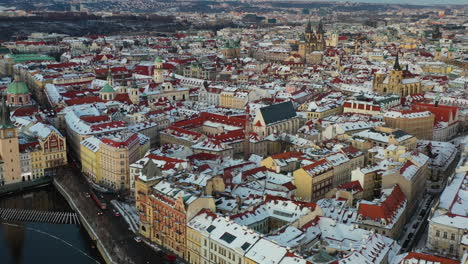 cinematic aerial view, prague old town at winter, snow on city buildings on cold evening, traffic by vltava river, czech republic, drone shot