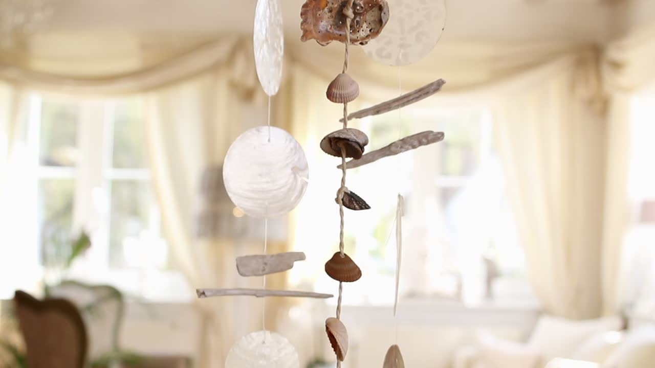 Ein Windspiel aus Muscheln in einem hell erleuchteten Wohnzimmer an einem sonnigen Morgen.