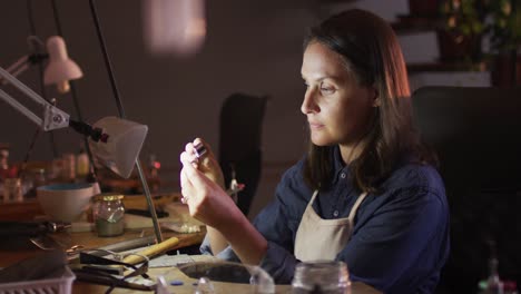 perfil de una joyera caucásica centrada sentada en un escritorio, haciendo joyas en un taller