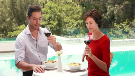 pareja sonriente bebiendo vino al lado de la piscina