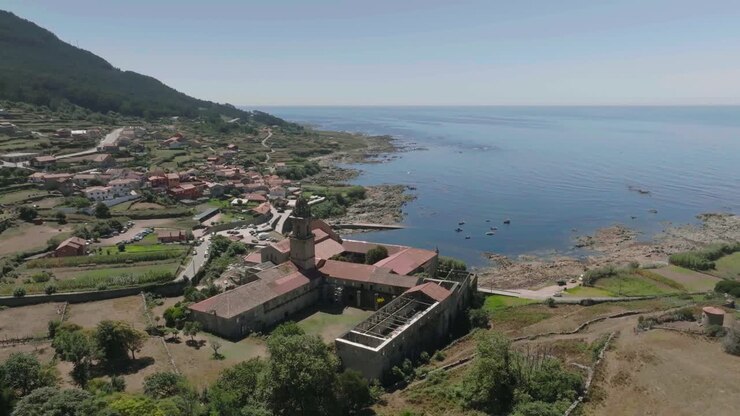 Ripresa aerea con drone in rotazione di un tetto danneggiato di un monastero storico situato a Santa María de Oia lungo la costa in una luminosa giornata di sole.