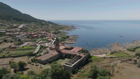 Aerial-drone-rotating-shot-of-damaged-roof-of-a-historic-monastery-located-at-Santa-Maria-de-Oia-along-the-seaside-on-a-bright-sunny-day