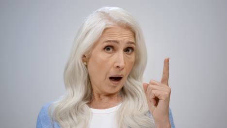 Thoughtful-old-woman-getting-idea-indoors.-Amazed-lady-opening-mouth-in-studio.