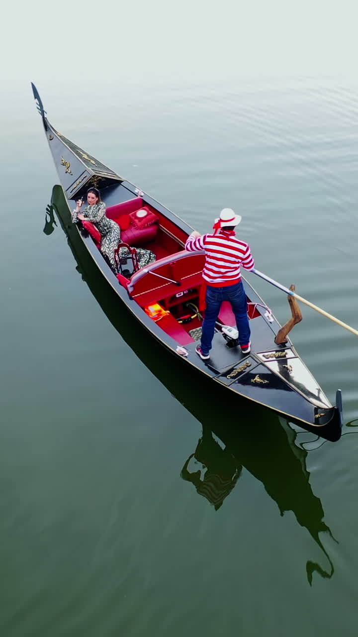 Beautiful woman sailing in gondola. Gondolier with oar moving boat slowly. Gondola floating the calm river in the evening. Vertical video
