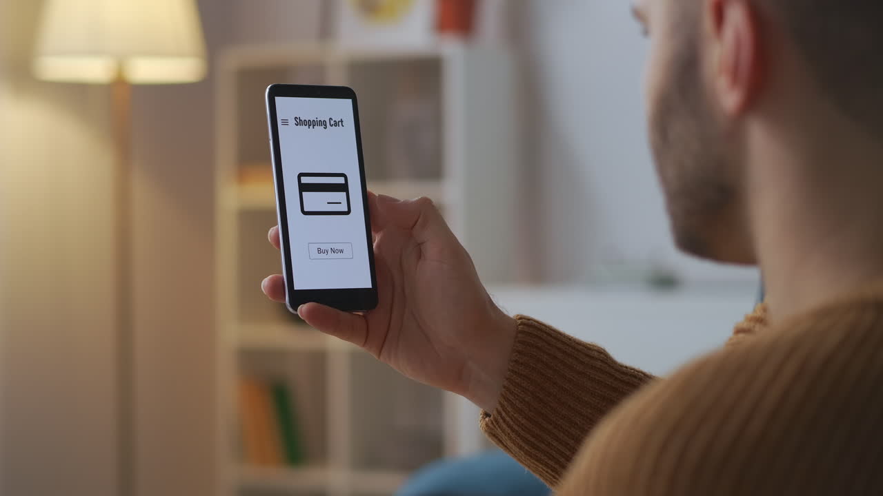 hombre está comprando en línea con su teléfono inteligente tocando la pantalla táctil pagando con una tarjeta gráficos en la pantalla vista a través del hombro del usuario sentado en casa