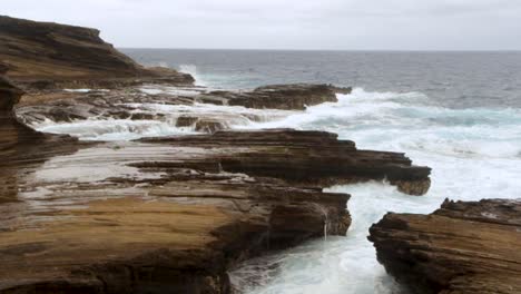 Waves-churn-and-crash-against-rock-formation-on-Hawaii-coastline,-slow-motion