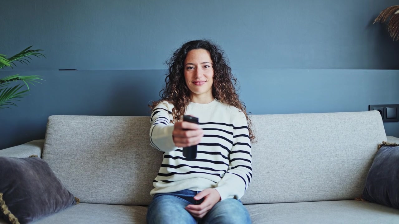 Young Woman Sitting on Sofa Using Remote Control
