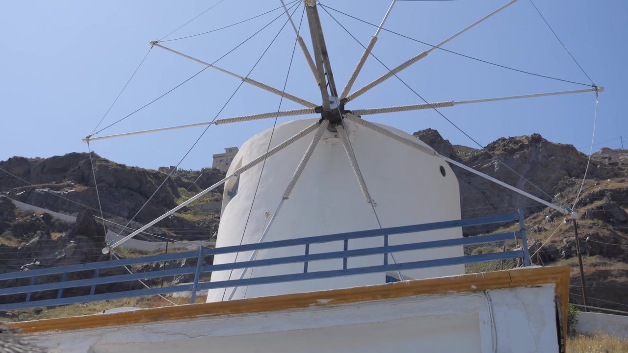 Iconico mulino a vento bianco sull'isola di Thirasia, Grecia, sotto un cielo azzurro limpido. Ripresa con tilt up.