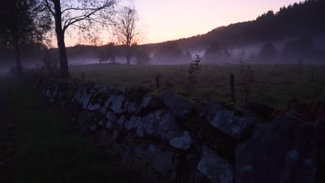 Die-Kamera-Folgt-Einer-Steinmauer-In-Der-Natur-Mit-Einem-Nebligen-Feld-Im-Hintergrund