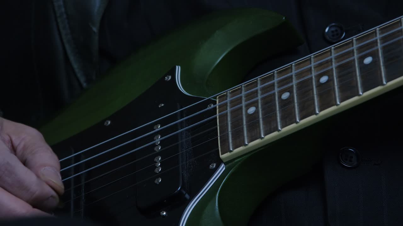 Electric guitar close up detail: Musician hand plays green SG, dark