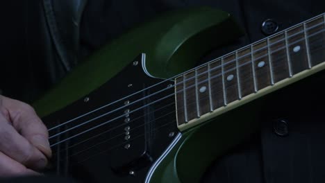 electric guitar close up detail: musician hand plays green sg, dark