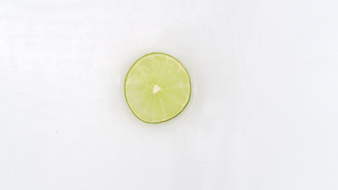en velocidad lenta salpicaduras de agua verter una lima sobre un fondo blanco. vegetarianos y fructorianos.