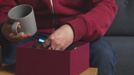 close up of man putting presents into gift wrapped box on table in lounge at home