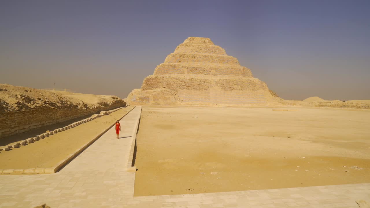 Žena v červených šatech kráčející směrem k Džoserově pyramidě v Sakkáře, Egypt