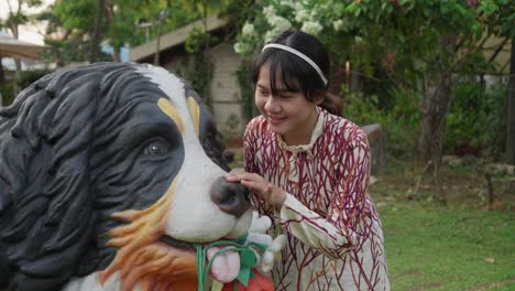 happy, youthful, and energetic young lady petting a st. bernard dog statue with a big smile on her face.