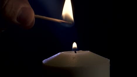 slow motion macro footage of a white candle lit by a match on a dark background