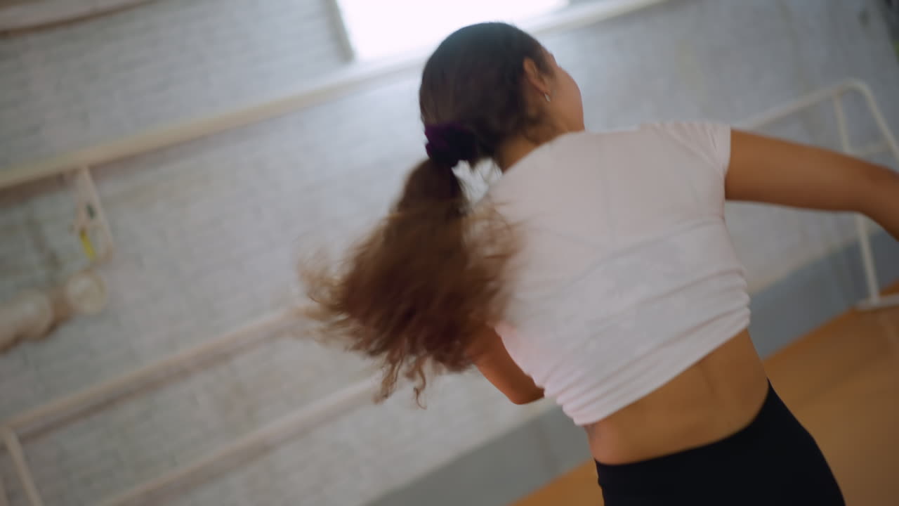 Close up view of woman in white top dancing energetically while flipping her hair inside fitness studio, showing focus, movement, and expressive spirit during active workout performance with joy
