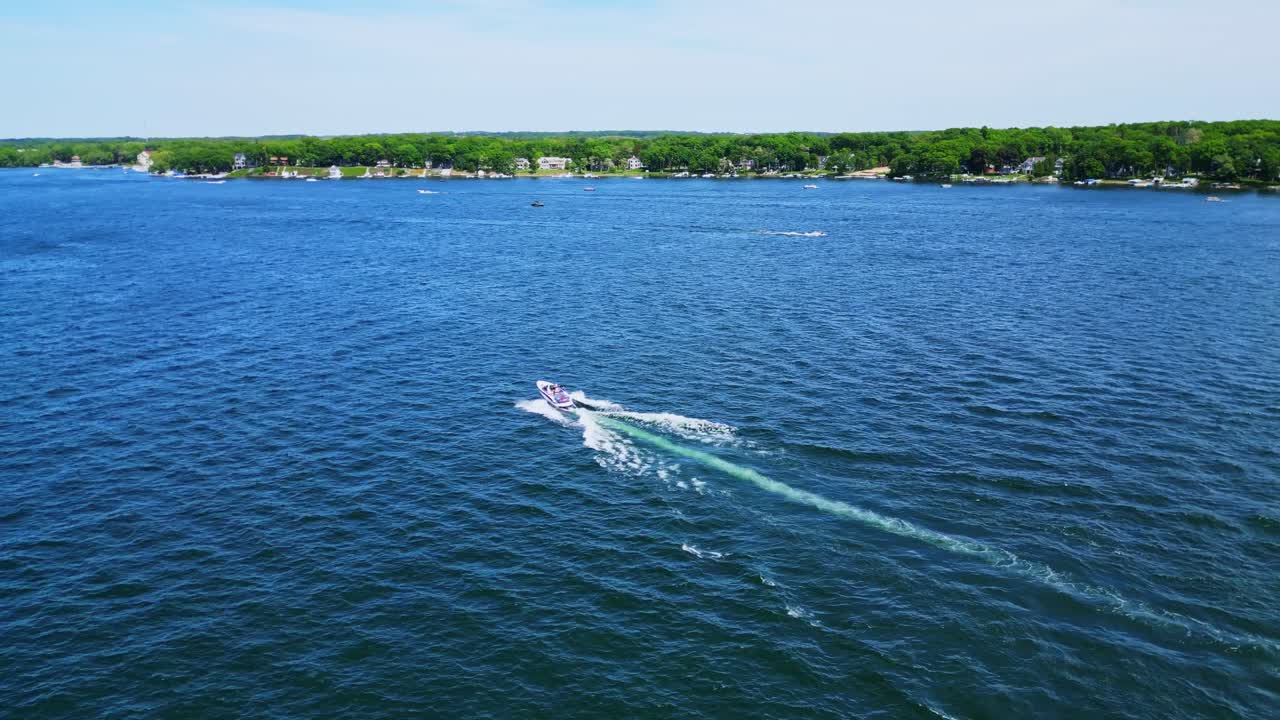 An aerial drone shot captures a speedboat cruising across the deep blue waters of Lake Delavan, leaving a foamy white and green wake behind it