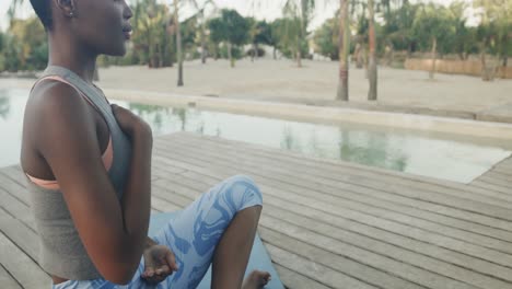 midsection of biracial woman practicing yoga meditation sitting on jetty, copy space, slow motion