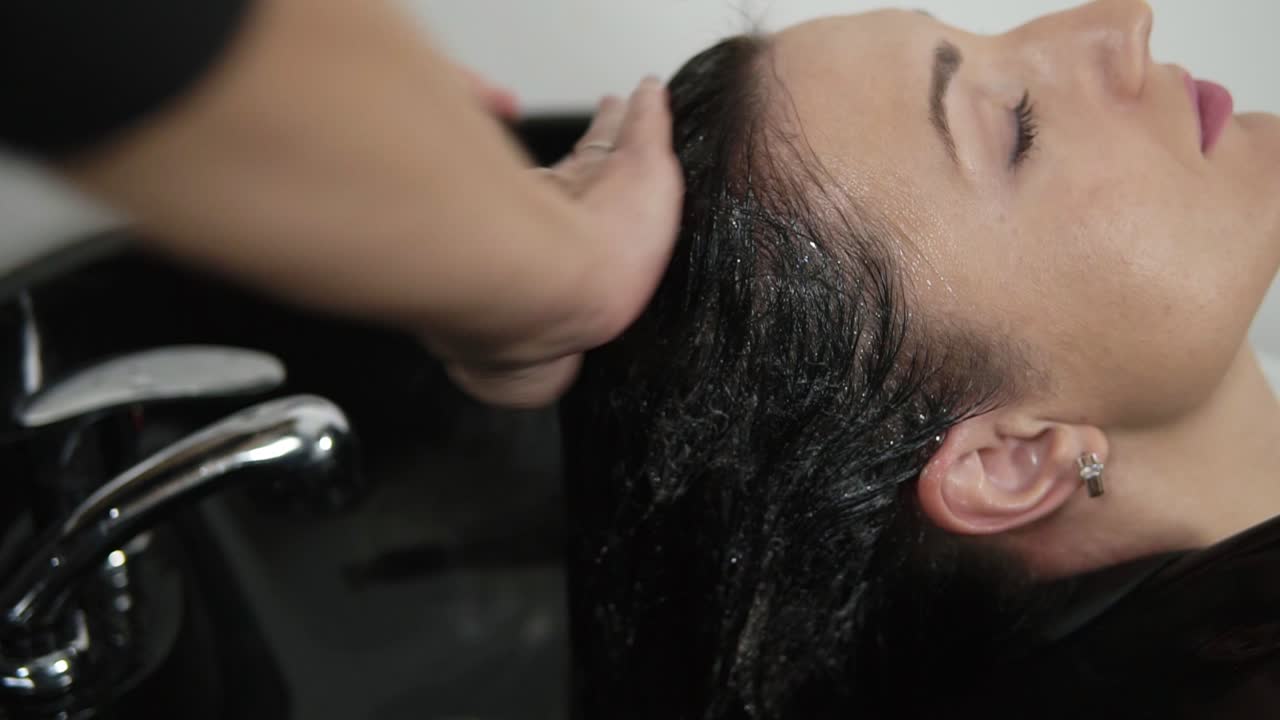 Hairdresser washing long haired woman and massaging shampoo into scalp before haircut. Hairdresser's hands wash head applying, foaming the shampoo on head. Close up