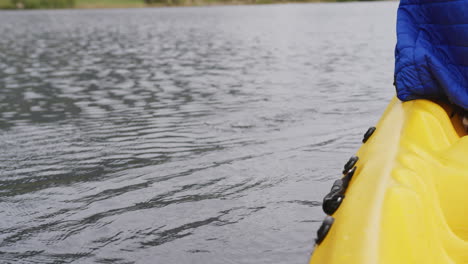 hombre caucásico pasando un buen rato en un viaje a las montañas, en kayak en un lago, sosteniendo un remo