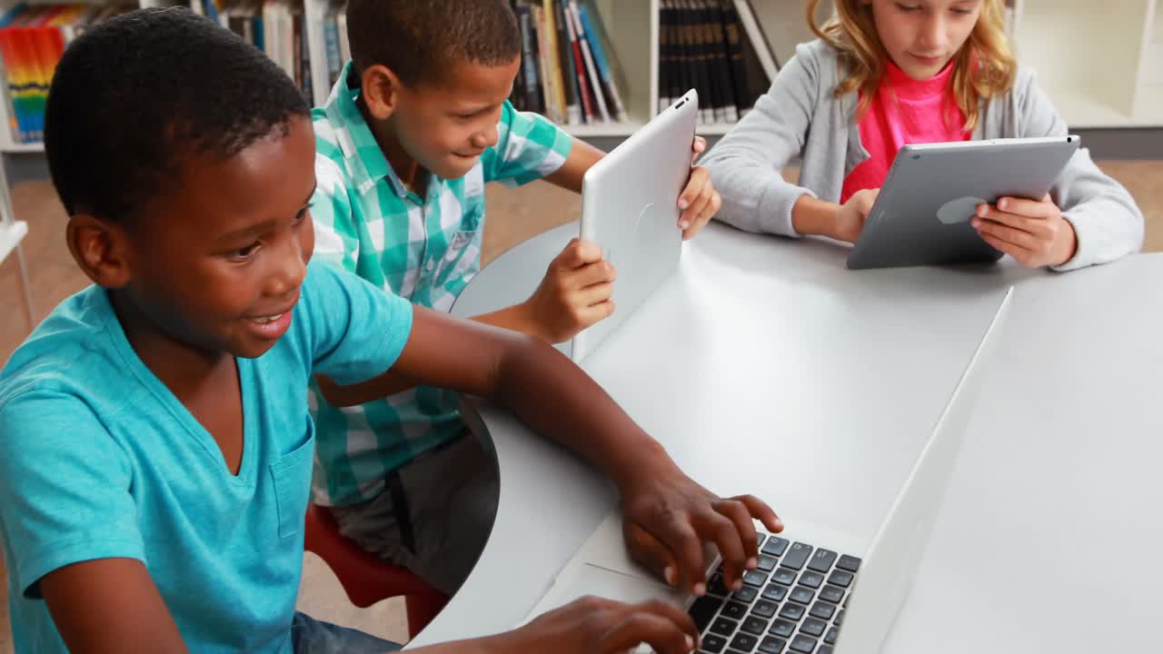 Group of school kids using digital tablet and laptop in library